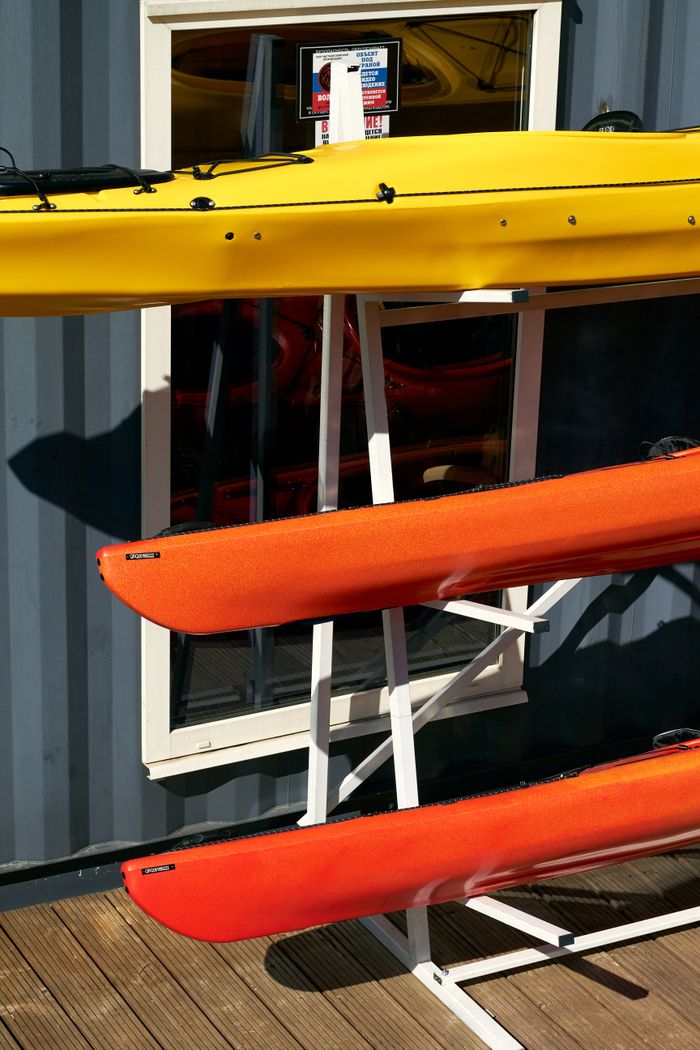 services-01 Bright yellow and orange kayaks stacked outside a warehouse in summer sunlight.