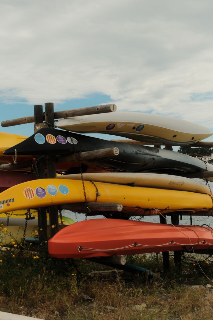 about-01 Stack of colorful kayaks on a rack outdoors against a cloudy sky, suggesting adventure or leisure activities.