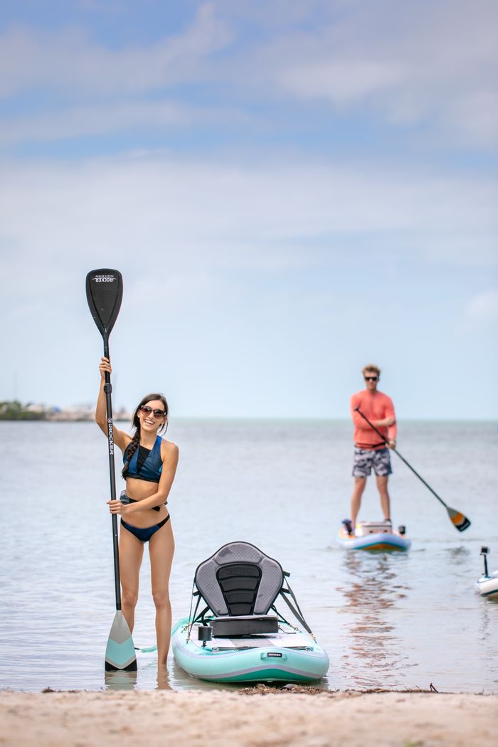 services-02 A man and woman paddle boarding on a sunny beach day, ideal for summer activities.